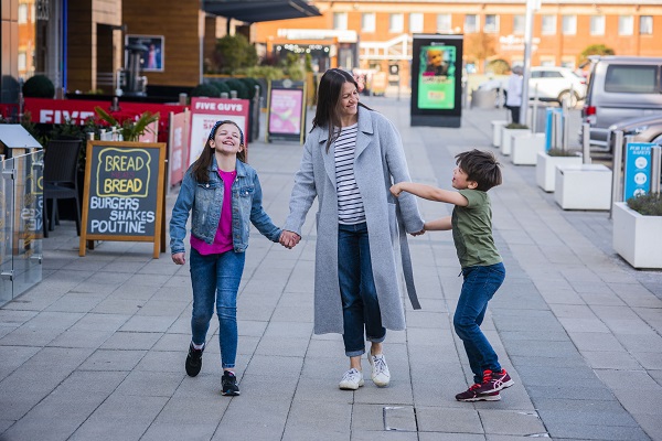 Mum smiling holding her son and daughter's hands and walking outside centre